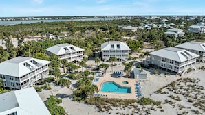 A coastal resort with multiple beachfront buildings, a central swimming pool, and a view of the ocean and distant shoreline.
