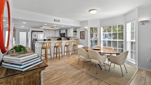 A modern kitchen with white cabinets, a central island, and a dining area with a wooden table and chairs.
