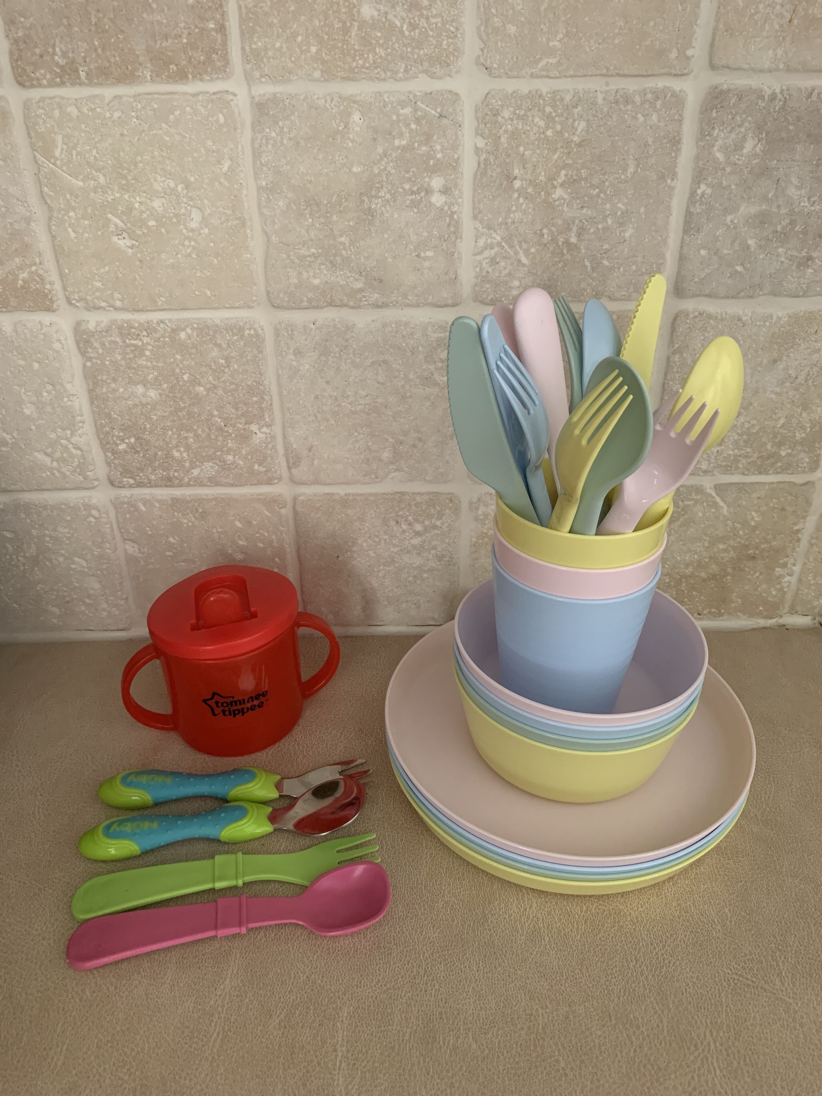 A kitchen counter with a stack of colorful plates and a cup holding utensils.