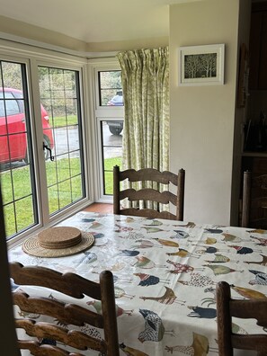 Enjoy meals in this cozy dining area with a table set for four, featuring a bird-patterned tablecloth and a wooden chair with a carved backrest.