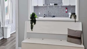 A modern kitchen with white cabinets, a herringbone backsplash, and a built-in bench with a plant and pillow.