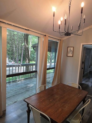 A dining area with a wooden table, white chairs, a chandelier, and large windows with curtains. - Getaway House at Avenwood Cabins (new straitsville)