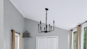 A dining area with a wooden table, white chairs, a chandelier, and a white door in the background.