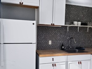 Una cocina con armarios blancos, salpicadero con motivo de espiga, encimera de madera y pileta de acero inoxidable.