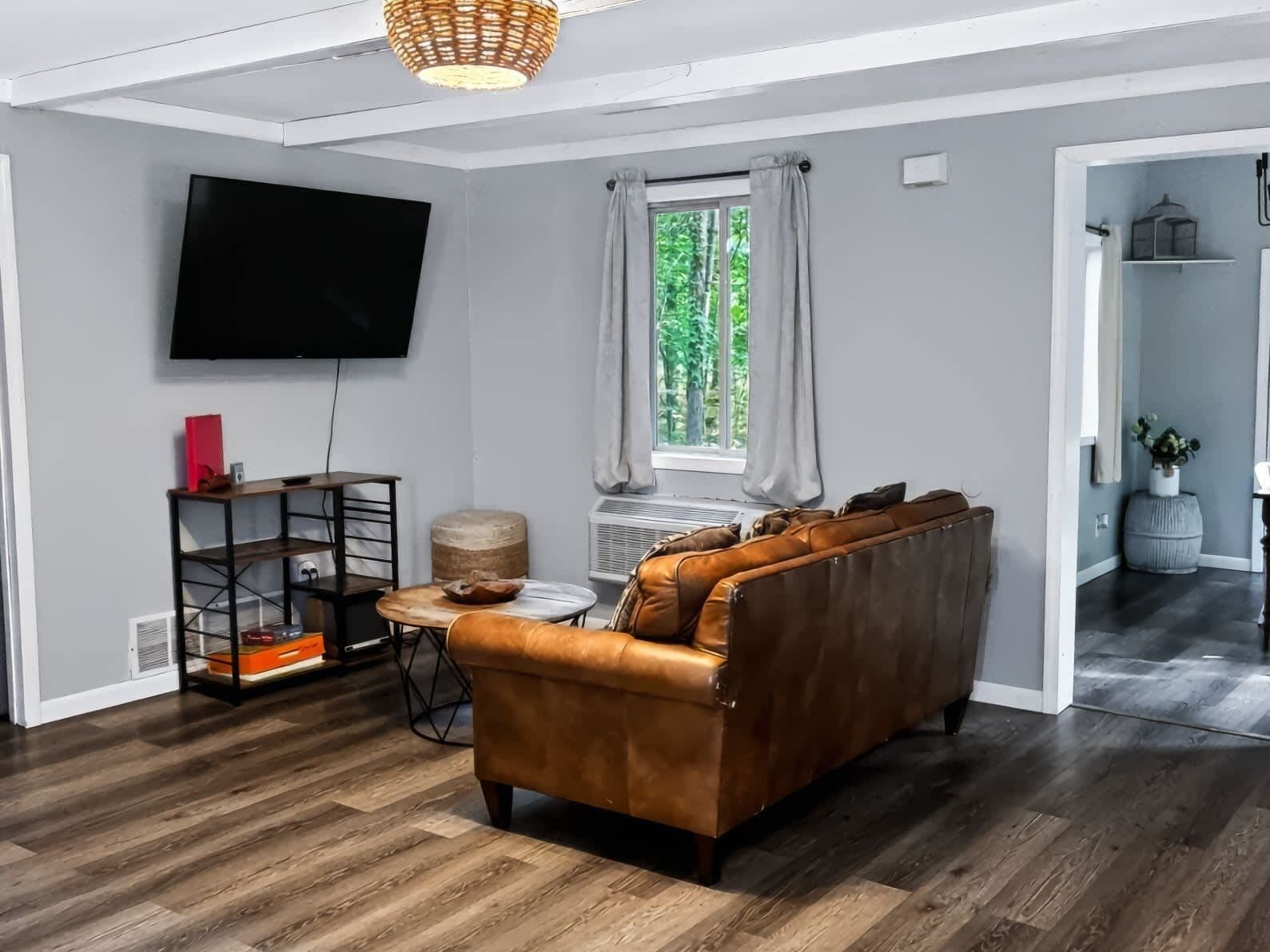 A modern living room with a leather sofa, a flat-screen TV, a wooden coffee table, and a window with curtains.