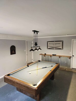 A pool table with a billiards sign, a framed warning sign, and a wooden shelf.