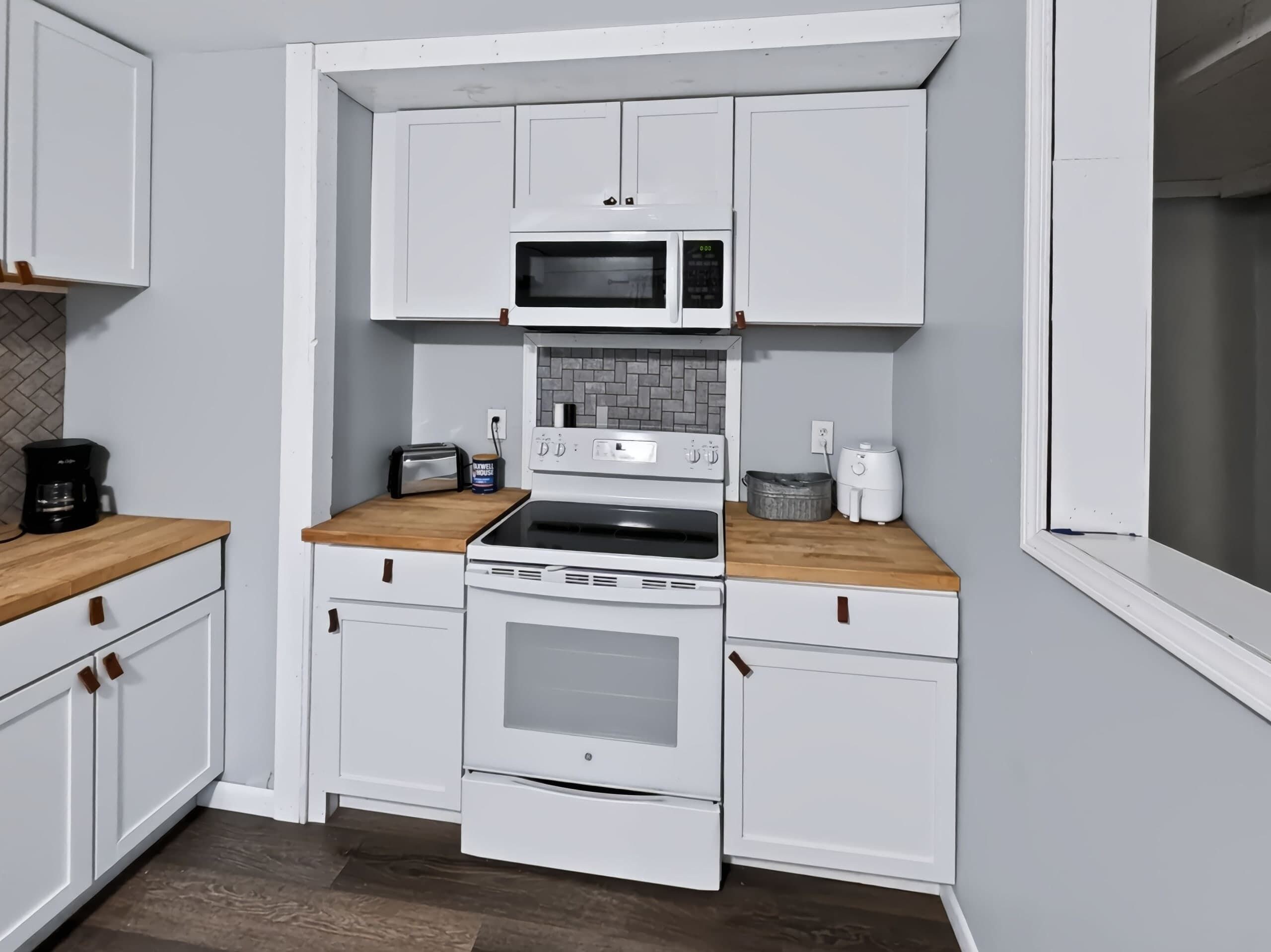Une cuisine de taille réduite avec des meubles blancs, un four à micro-ondes, un grille-pain et une cuisinière.