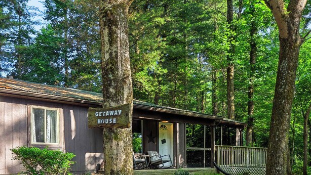 A cabin with a porch, surrounded by trees and a gravel path.