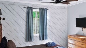 A bedroom with a bed, a dresser, a TV, a ceiling fan, and a window with curtains.