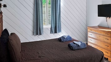 Una camera da letto con un letto, una cassettiera, una TV, una ventola a soffitto e una finestra con tende.