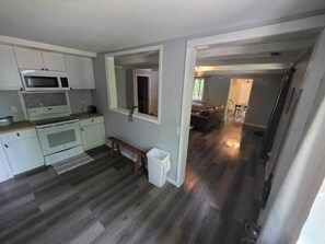 A kitchen with a microwave, oven, and bench, leading to a living area with a couch and a visible door. - Getaway House at Avenwood Cabins (new straitsville)