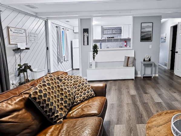 A modern living room with a brown leather sofa, a white sofa with a patterned cushion, and a small round table.