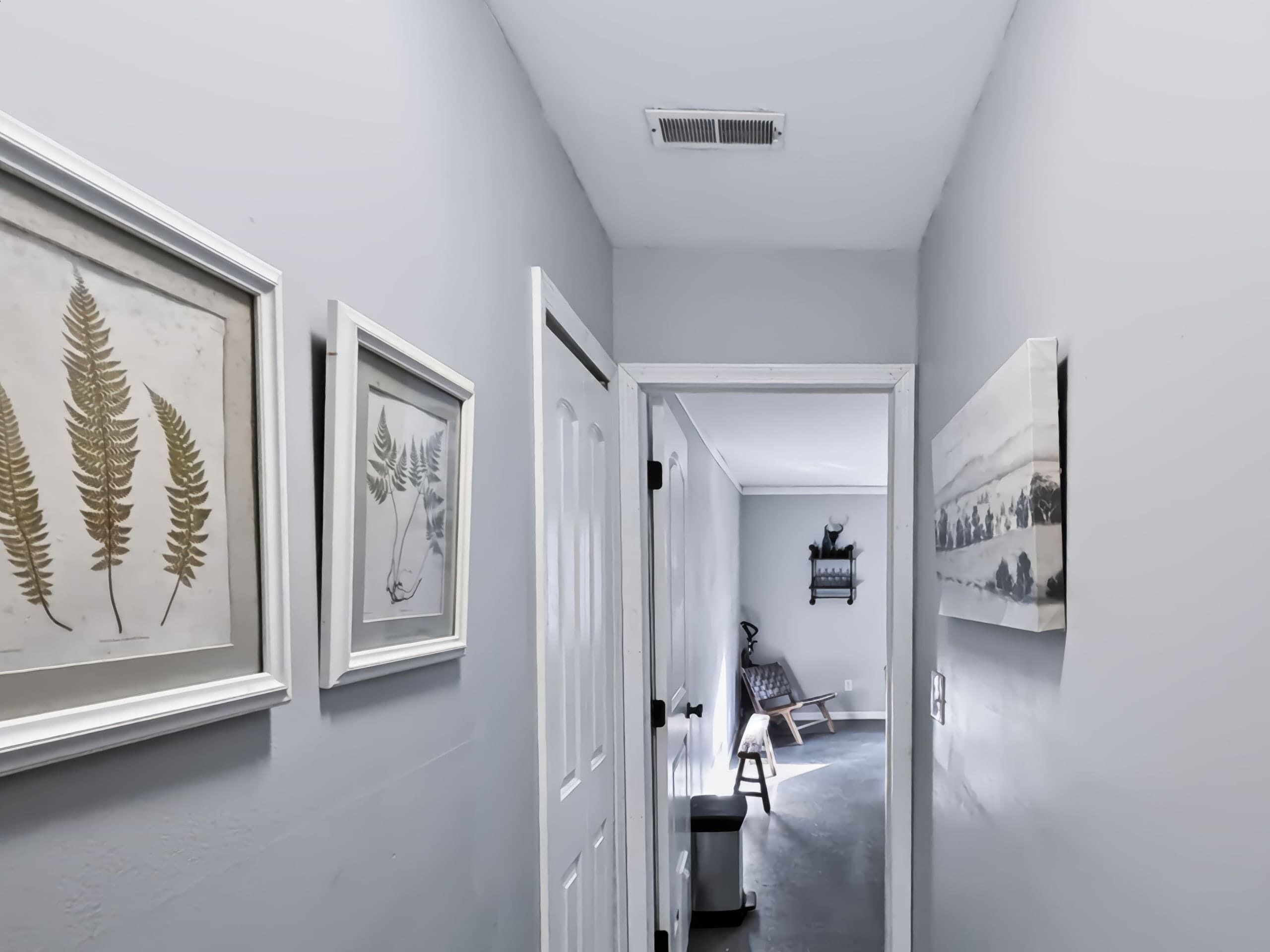 A hallway with framed botanical prints on the walls, a door leading to another room, and a chair in the distance.