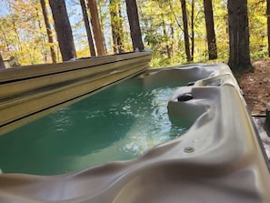A hot tub in a forested area with a view of trees and a clear sky. - Getaway House at Avenwood Cabins (new straitsville)