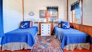 Une chambre avec deux lits, une commode, un tapis et une fenêtre avec des rideaux.