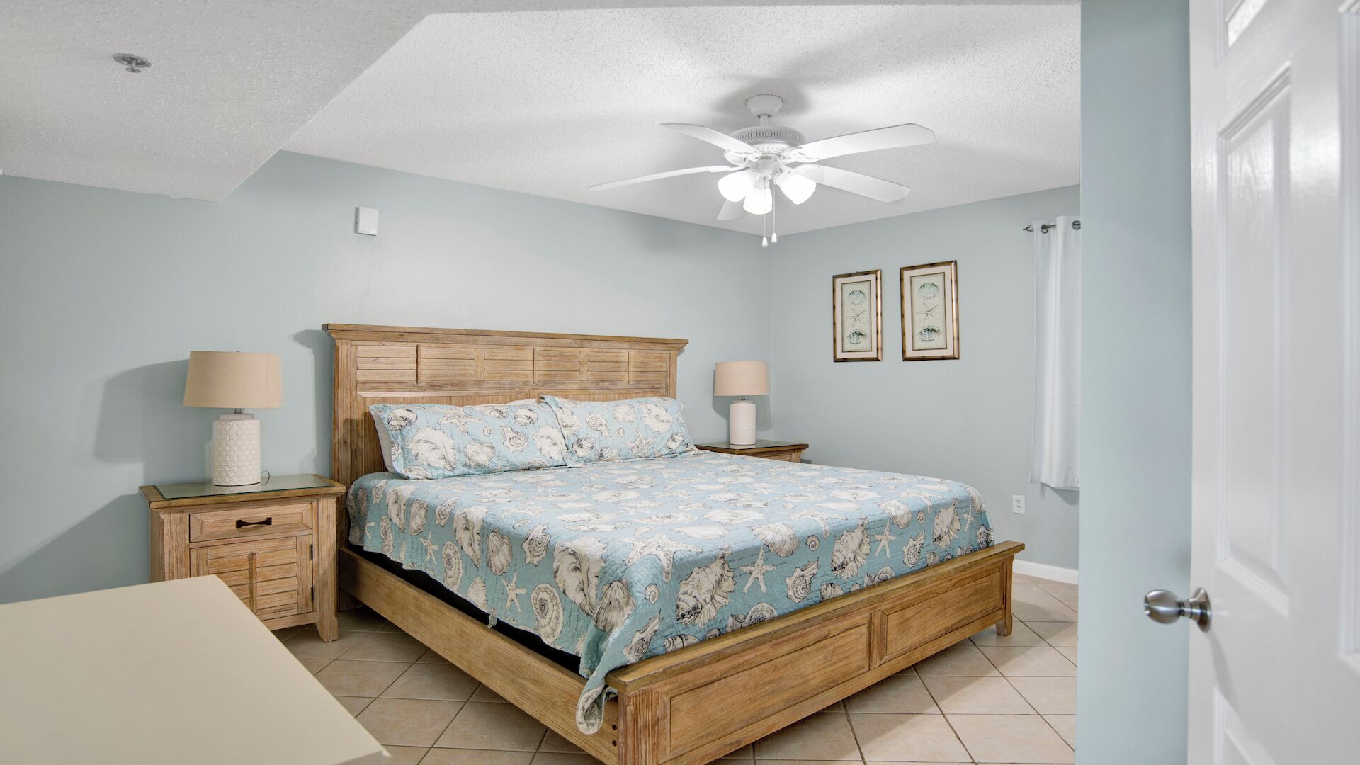 A bedroom with a wooden bed, two bedside tables, a ceiling fan, and two framed pictures on the wall.