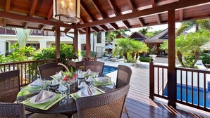 A covered outdoor dining area with wicker furniture and a pool in the background. - Villa Alila  Summer Promotion | Near Ocean - Located in  Tropical Sandy Lane with Private Pool (Holetown)