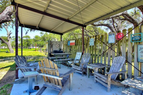 An outdoor patio with wooden chairs and tables, a barbecue grill, and a covered area with a metal roof.