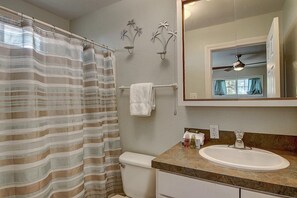 A bathroom with a striped shower curtain, a toilet, a sink with a marble countertop, a towel rack, and a wall-mounted mirror.