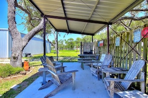 An outdoor patio with wooden chairs and a grill, surrounded by a wooden fence and trees.