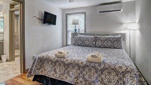 Une chambre avec une couvre-lit à motifs, un ventilateur de plafond, un appareil de climatisation, un téléviseur fixé au mur et une fenêtre donnant sur un beau paysage.