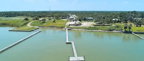 A riverside view with a dock extending into the water, surrounded by greenery and a clear sky.