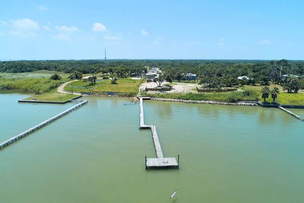 Uitzicht op een rivier met een steiger die het water in reikt, omringd door groen en een heldere lucht.