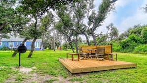 Une terrasse en bois avec des meubles d’extérieur, un barbecue et une maison en arrière-plan.