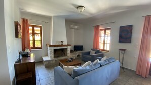 A living room with a stone fireplace, blue sofa, and a television. - Executive Villa Madouri With Private Pool (Lefkada)