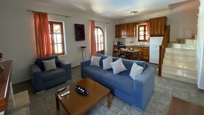 A living room with a blue sofa, a wooden coffee table, and a kitchen in the background. - Executive Villa Madouri With Private Pool (Lefkada)