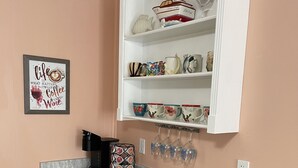 A kitchen with a marble countertop, a coffee maker, a knife block, and a shelf with decorative items.