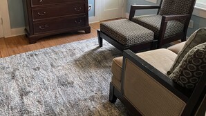 A living room with a dark wooden dresser, a television, patterned chairs, and a gray rug.