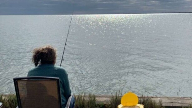 A person fishing by a calm body of water with a clear sky.