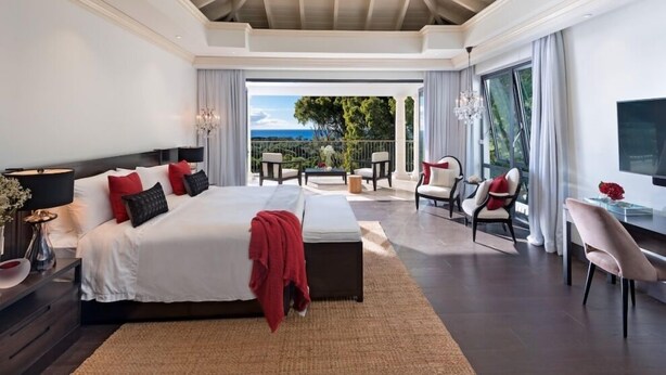 A spacious bedroom with a large bed, a balcony with outdoor furniture, and a TV. - Villa Elsewhere  | Ocean View - Located in  Stunning Sandy Lane with Private Pool (Holetown)