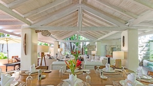 A dining area with a wooden table set for a meal, surrounded by a covered patio with a view of the outdoors. - Landmark House & Cottage  Summer Promotion | Beach Front - Located in  Exquisite Saint James with Private Chef Services (Saint James)
