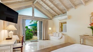 A bedroom with a large bed, a desk with a lamp, a TV, and a window overlooking a garden. - Landmark House & Cottage  Summer Promotion | Beach Front - Located in  Exquisite Saint James with Private Chef Services (Saint James)