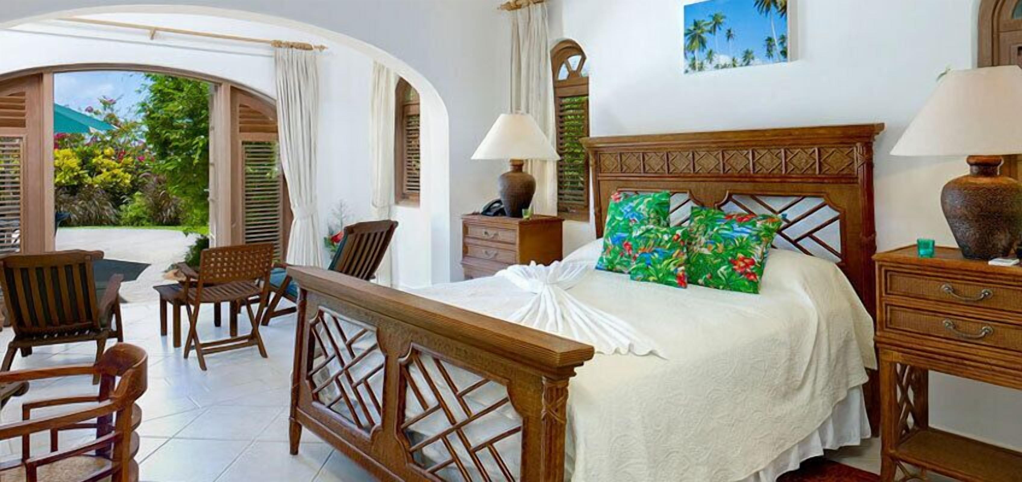 A bedroom with a wooden bed, two bedside tables, a nightstand, a chair, and a view of the garden.