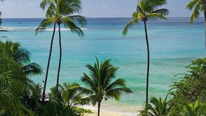 A beach with clear turquoise water, palm trees, and a distant view of boats. - Schooner Bay 108 - Condo Chilterns | Beach Front - Located in  Magnificent St. Peter with Concierge Services (St. Peter)