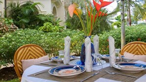 A table set for dining outdoors with wicker chairs, a white tablecloth, and a vase with red flowers. - Schooner Bay 108 - Condo Chilterns | Beach Front - Located in  Magnificent St. Peter with Concierge Services (St. Peter)