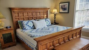 Uma cama de madeira com colcha, um criado-mudo com luminária e uma janela com persianas.