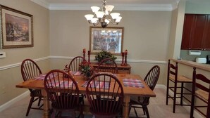 Uma sala de jantar com uma mesa de madeira, seis cadeiras, um candelabro e quadros nas paredes.