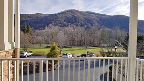 Uma varanda com vista para um estacionamento, uma montanha e um campo de golfe.