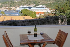 A table with two chairs and a bottle of wine, overlooking a cruise ship and a coastal town.