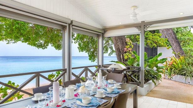 A dining area with a view of the sea, a table set with white plates and blue napkins, and a ceiling fan.
