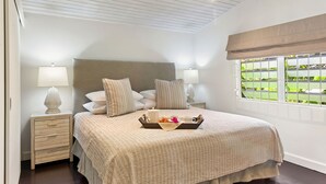 A bedroom with a large bed, two bedside tables with lamps, a tray with breakfast items, and a window with a view of greenery.