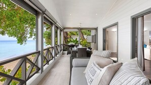 A balcony with a view of the sea, a dining area, and a seating area with a sofa and pillows.