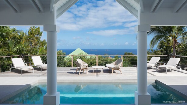 Un espace aménagé au bord de la piscine, avec des chaises longues, une vue dégagée sur l’océan et une structure couverte.