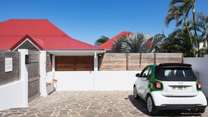 Une villa avec un toit rouge, une allée pavée de pierres et une voiture blanche garée dans l’allée.