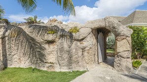 Un arc de pedra que condueix a un edifici, envoltat d'un jardí ben cuidat i palmeres.