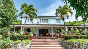 Une maison à deux étages dotée d’un porche abrité, d’un escalier en pierre et d’un aménagement paysager de style tropical.